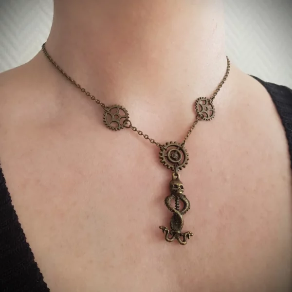 Ce collier steampunk couleur bronze est composé d'engrenages et d'un caducé tête de mort et serpents en pendentif central.