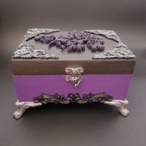 Dans les tons argenté, violet et noir, cette boîte en bois décorée Féerie baroque est une avalanche d'arabesque, empli de détails jusqu'aux pieds.