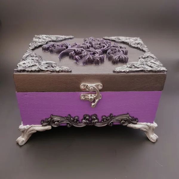 Dans les tons argenté, violet et noir, cette boîte en bois décorée Féerie baroque est une avalanche d'arabesque, empli de détails jusqu'aux pieds.