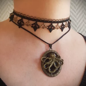 Ce collier steampunk en dentelle avec pendentif est composé d'une partie ras du cou en dentelle noire et doré ancien de style baroque, accompagné par un pendentif pieuvre soutenu par un cordon satiné noir.