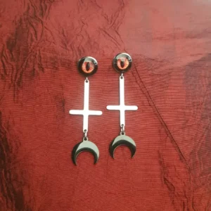 Ces boucles d'oreilles Lilith mère des démons arbore oeil démoniaque et croix satanique, avec finition croissant de lune noire. En acier inoxydable.