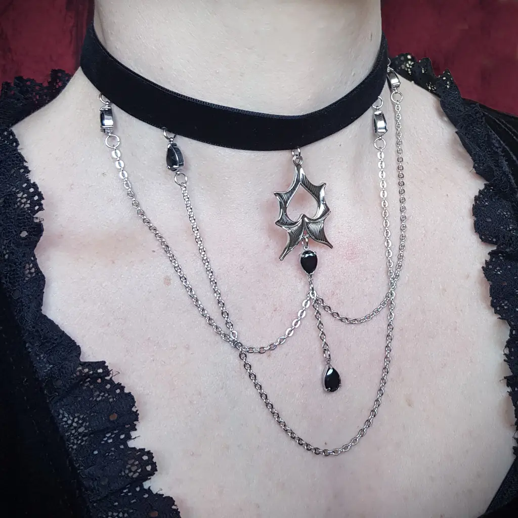 Ce collier chauve souris gothique en acier inoxydable va faire tourner des têtes! Avec ses ailes déployés, ses multiples chaines pendantes le tout orné de touches de verre noir, voici un collier gothique ras le cou qui illustre l'élégance sombre.